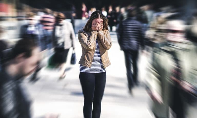 young woman in crowd covering face 768: Panic disorders are when an individual has sudden bursts of sheer panic and intense fear that are typically in response…